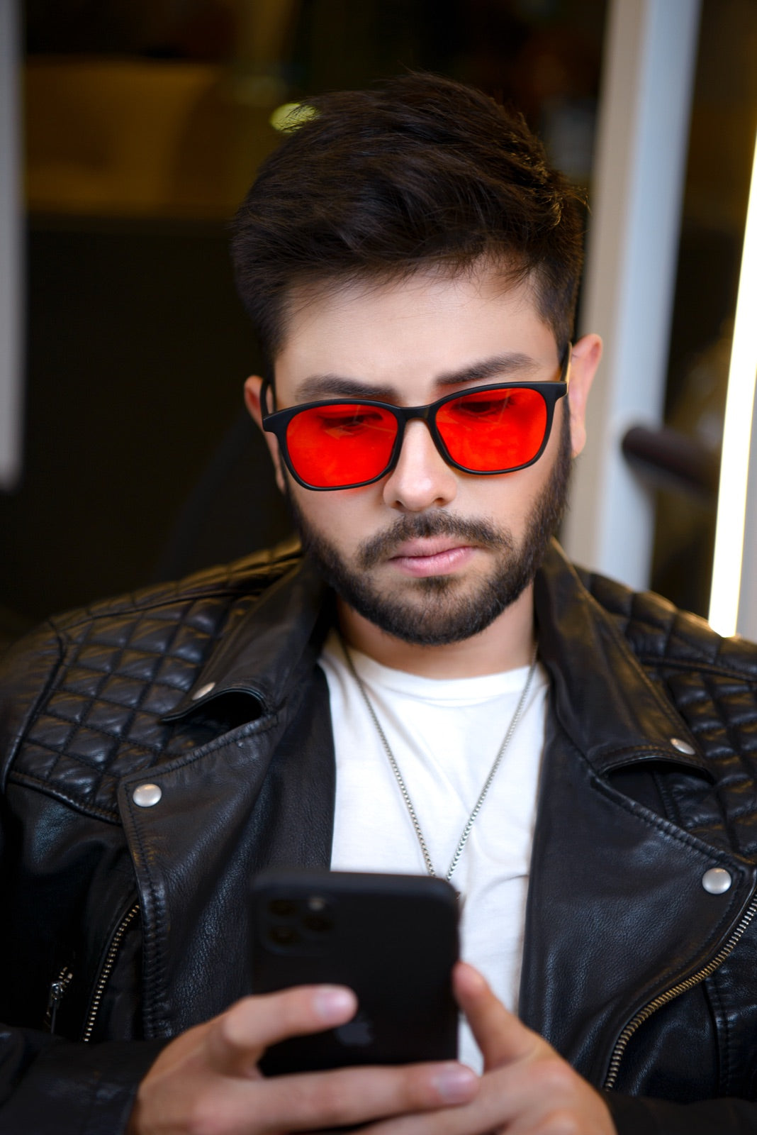 Hombre con chaqueta de cuero mirando su celular de noche con los lentes Alpha + Sueño puestos
