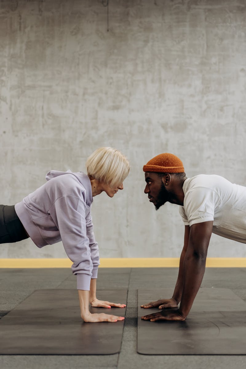 Hombre y mujer haciendo flexiones cara a cara en gimnasio