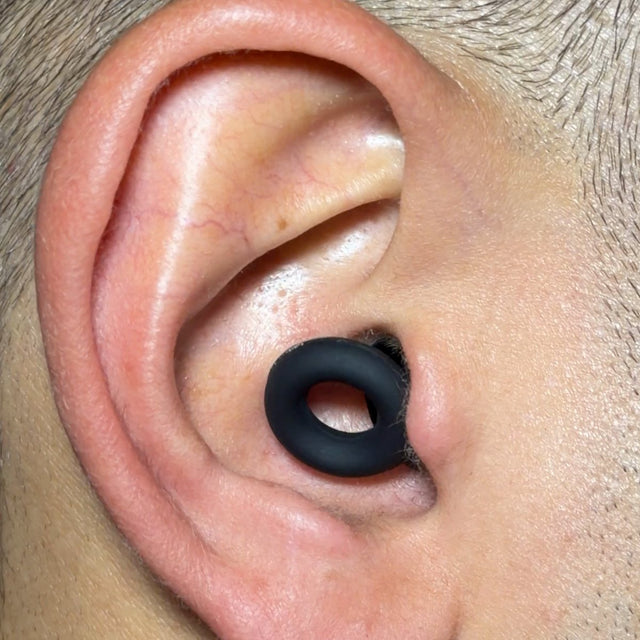 Primer plano de una oreja con el tapón puesto: el aro negro queda acomodado en la base de la oreja, sin sobresalir.