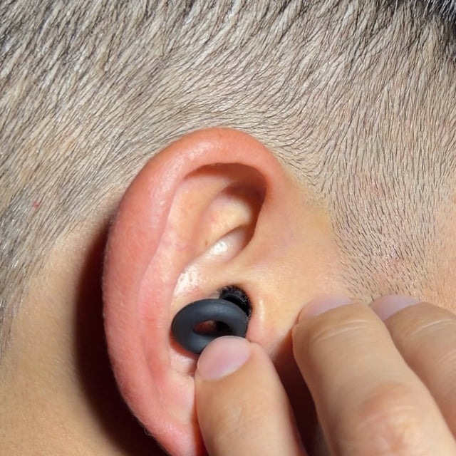 Primer plano: el pulgar y el índice toman el aro del tapón puesto en la oreja.