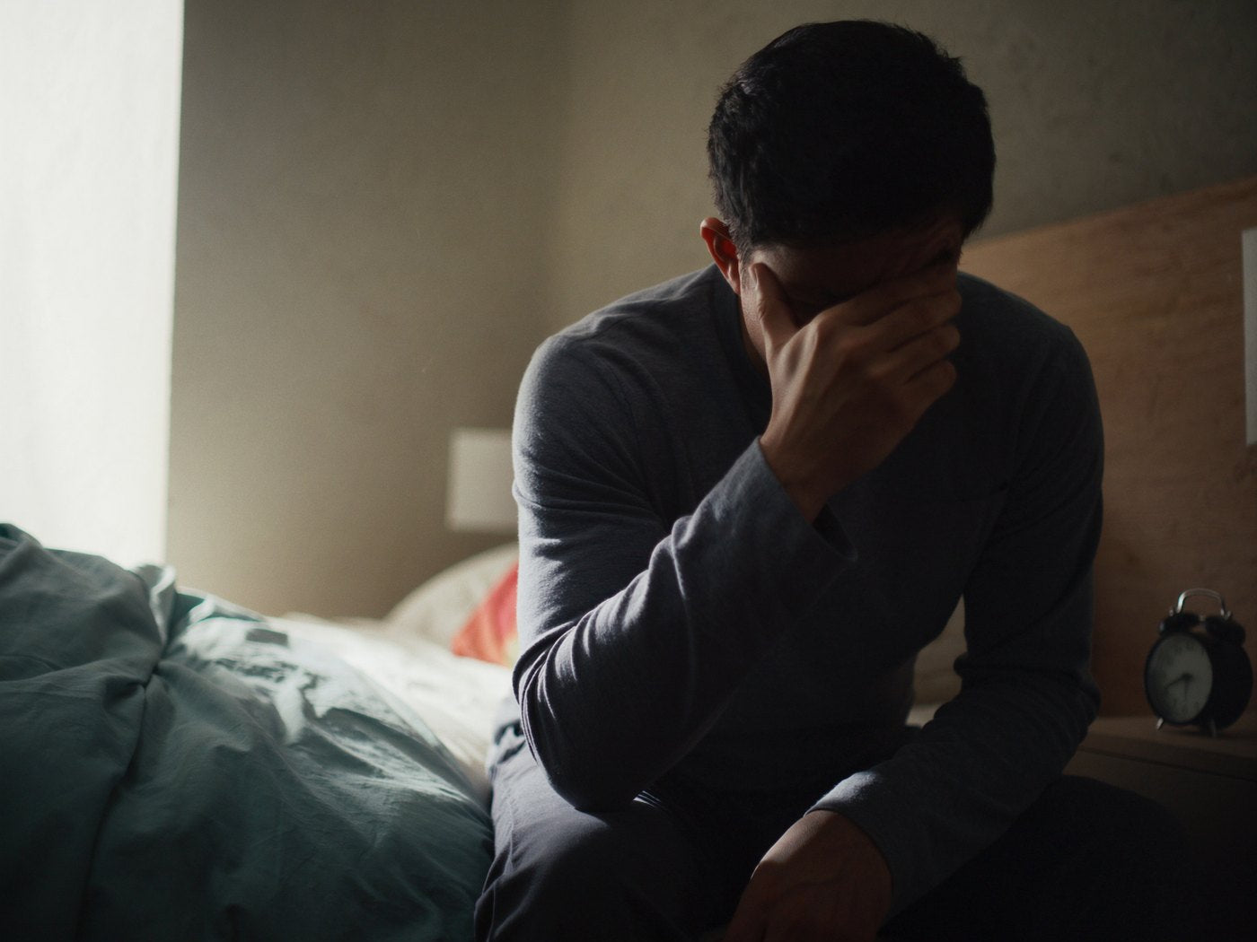 Hombre agotado sentado al borde de la cama por la mañana, junto al despertador