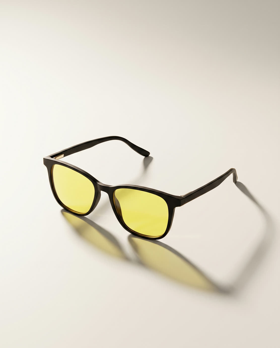 Lentes Alpha Clarity en tres cuartos sobre fondo hueso: montura negra mate con lente amarillo