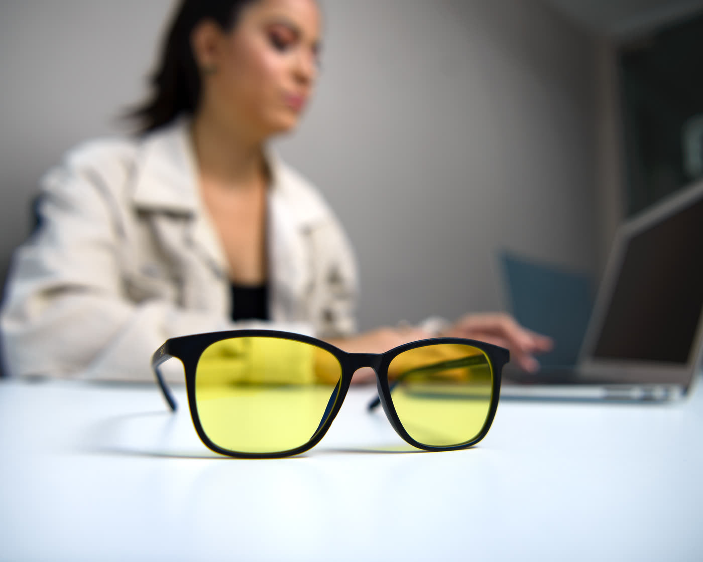 Lentes Alpha Clarity sobre un escritorio con una mujer trabajando en su laptop al fondo