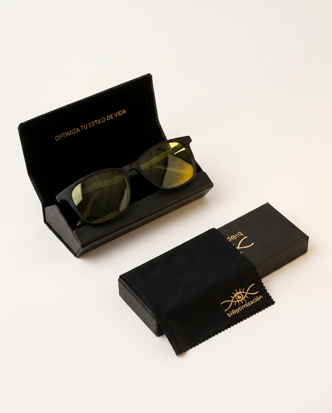 Lentes Alpha Clarity sobre su estuche rígido negro, junto al paño con logo dorado y la caja de biOptimización
