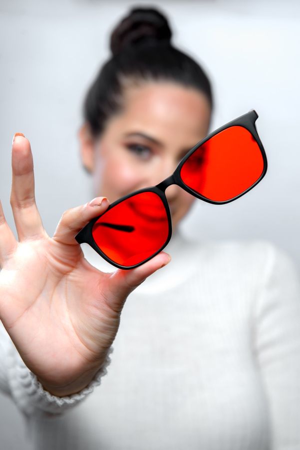 Mujer sosteniendo los lentes Alpha + Sueño hacia la cámara: el lente rojo en primer plano