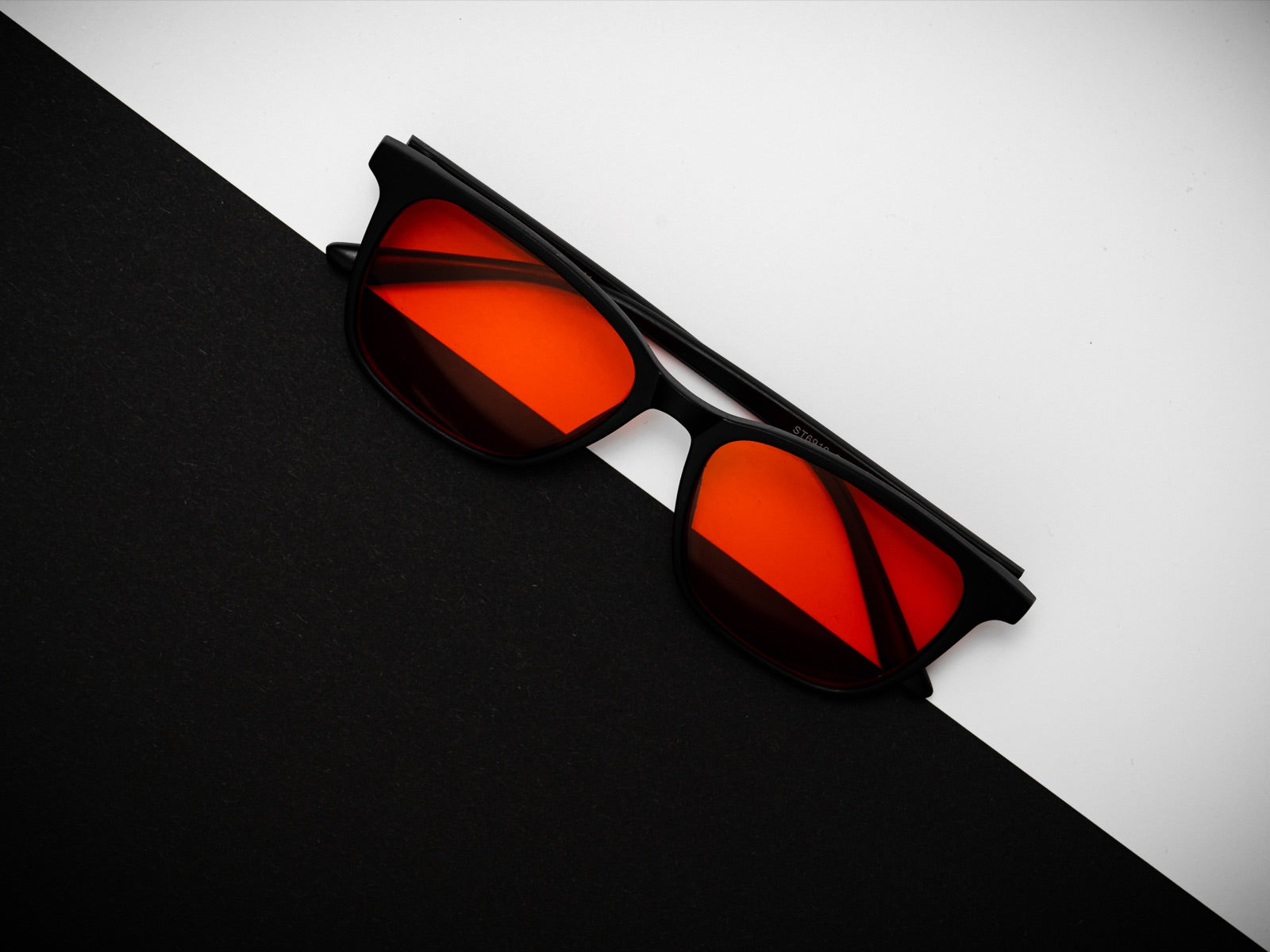 Lentes Alpha + Sueño sobre un fondo diagonal negro y blanco, vista editorial del lente rojo