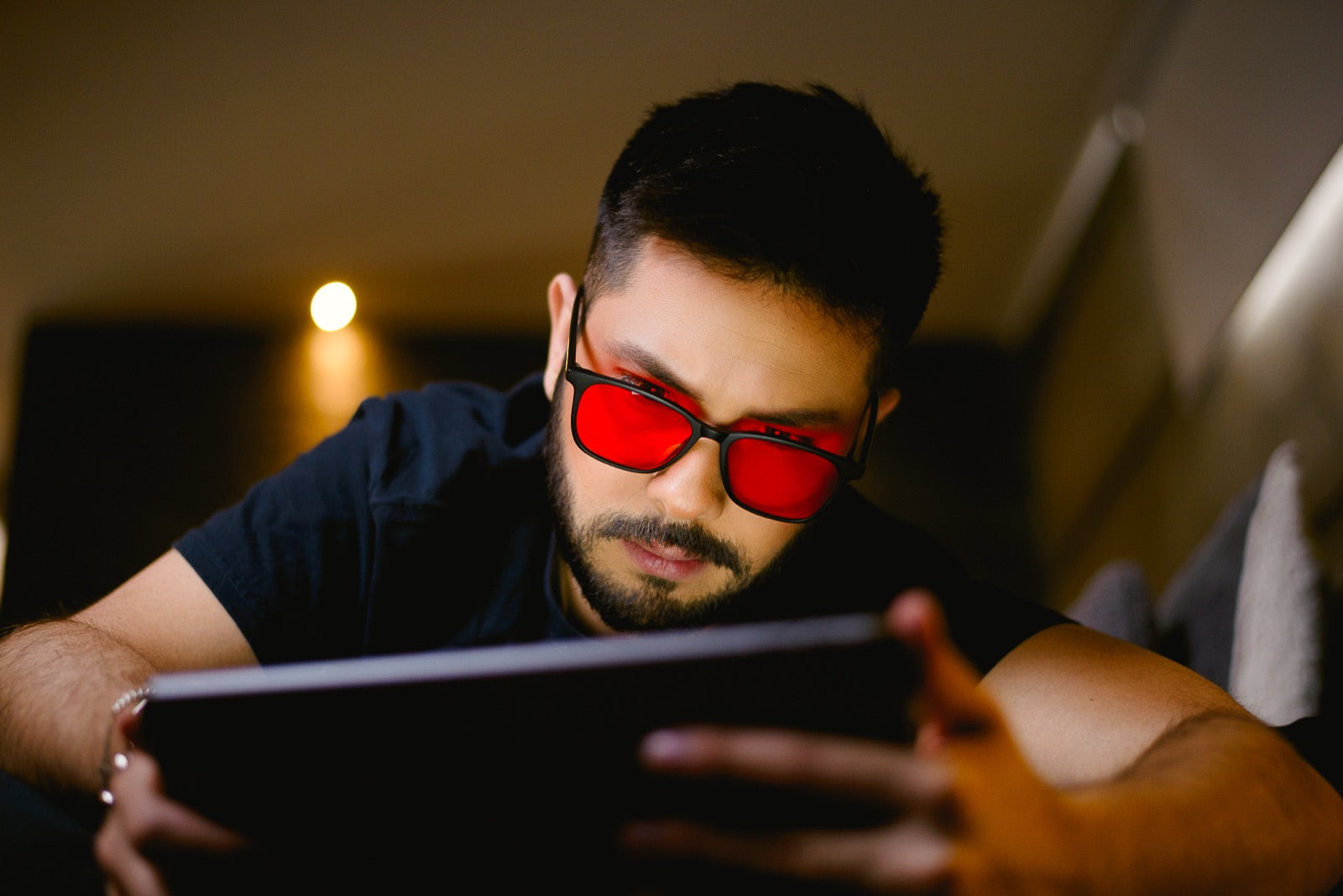 Hombre recostado en su cama de noche usando una tablet con los lentes Alpha + Sueño puestos